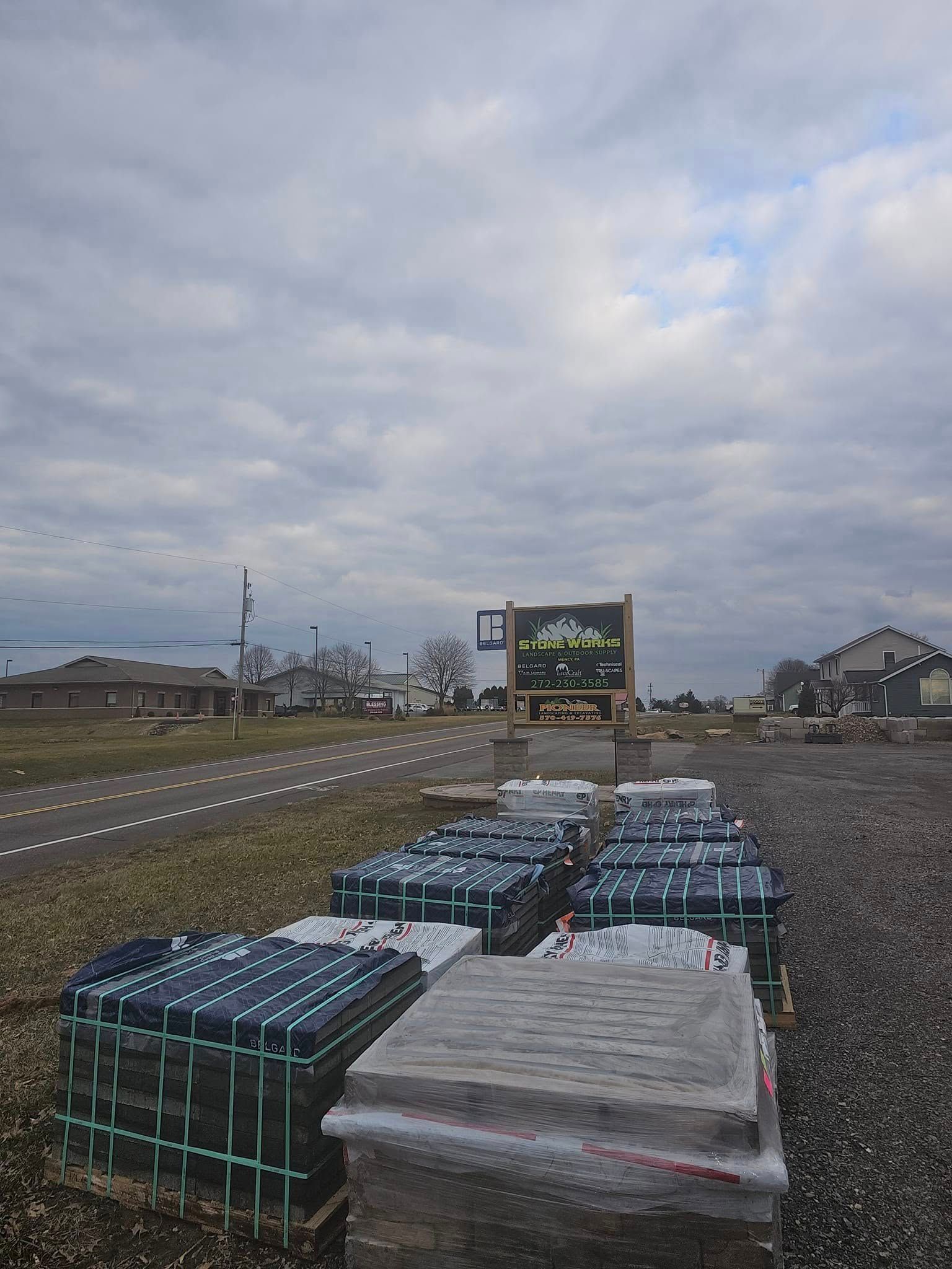 Stacks of wrapped pallets in a gravel lot beside a road under a cloudy sky.