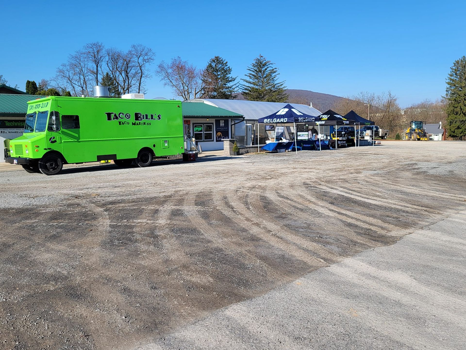 Bright green service truck parked beside a building and tents in a gravel lot under a clear blue sky