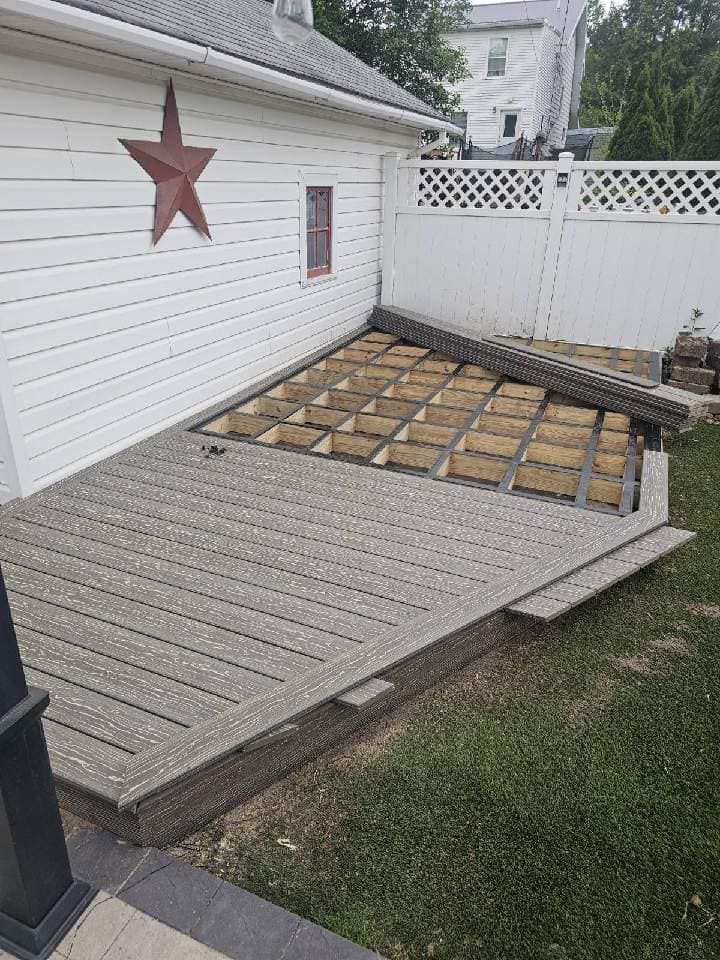 Backyard deck with a ramp leading to a raised platform, beside a white house and fence