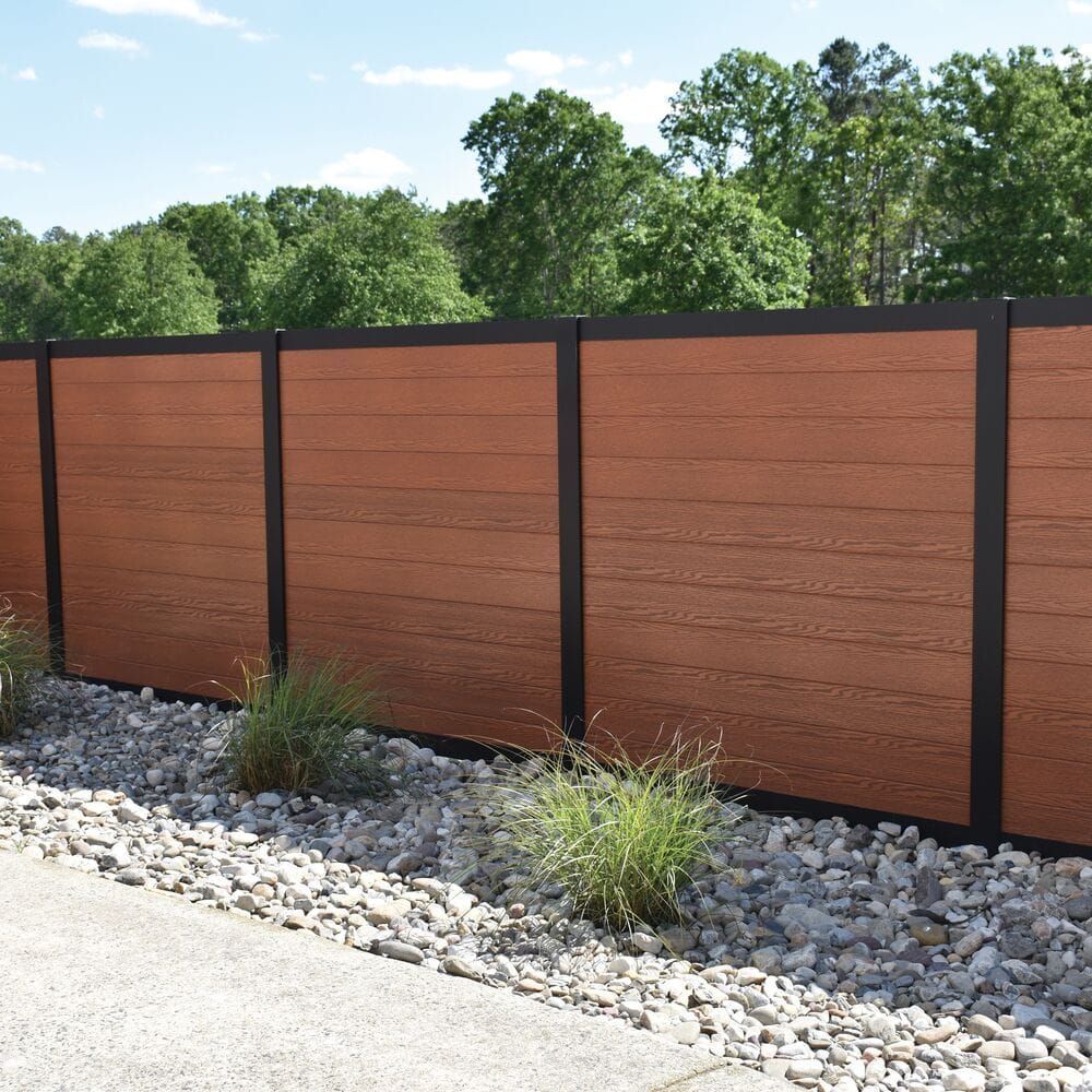 Modern privacy fence with dark posts, rust-colored panels, and gravel landscaping beside a sidewalk.