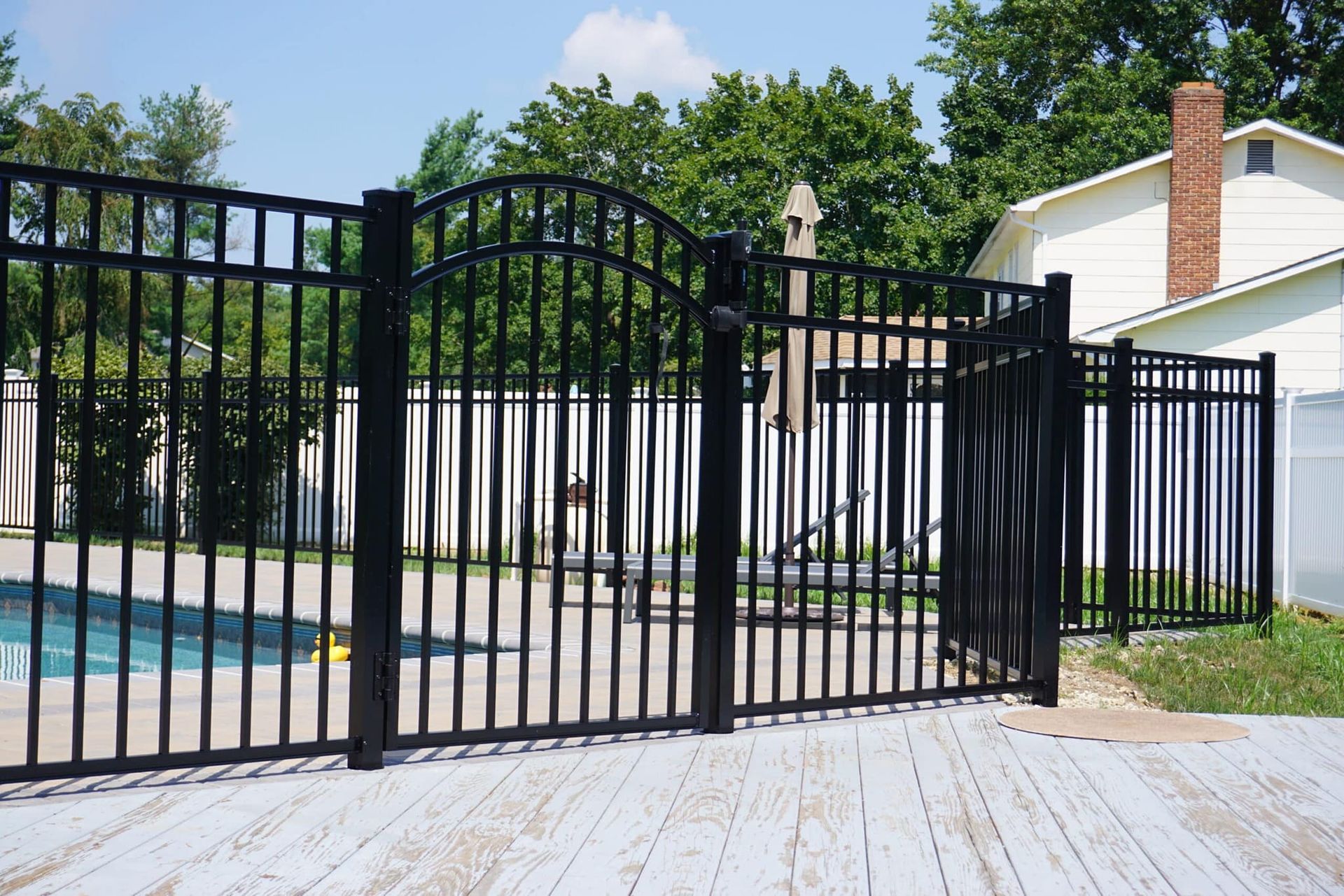Black metal gate beside a backyard pool and white house in a sunny yard