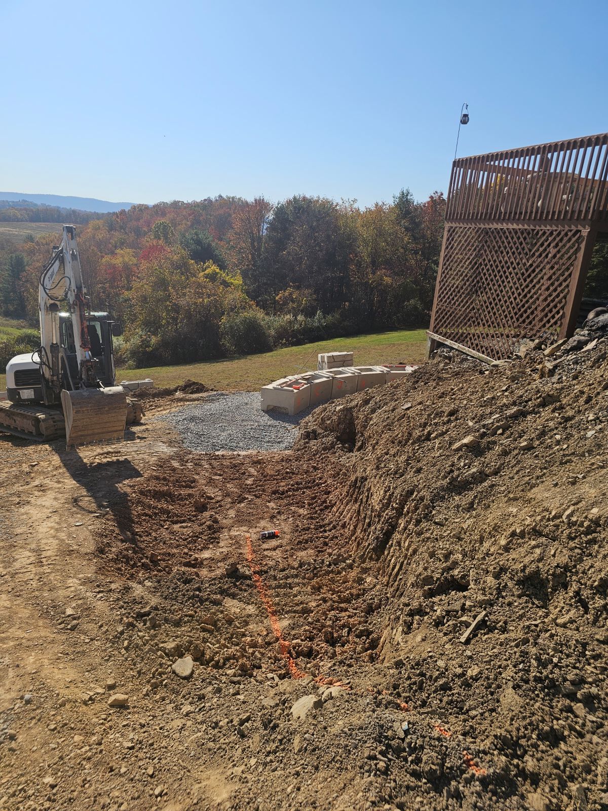 Excavator grading a dirt slope beside a retaining wall on a sunny hillside under construction