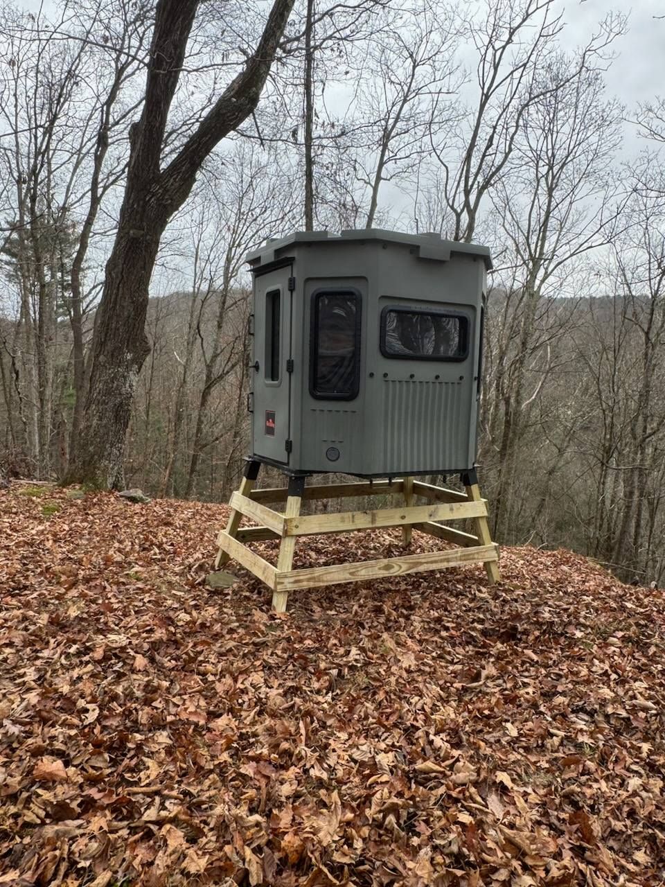 Gray hunting blind on wooden platform in leaf-covered woods
