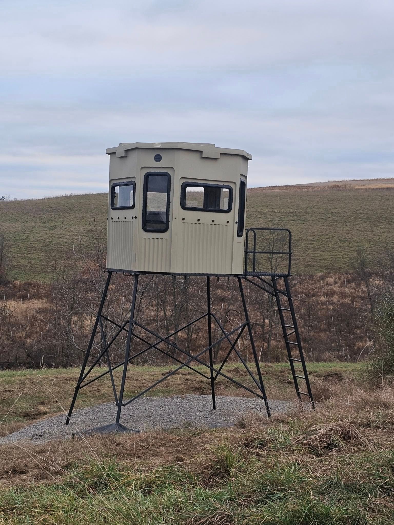 Small gray lookout cabin on tall metal stilts in a barren field under an overcast sky