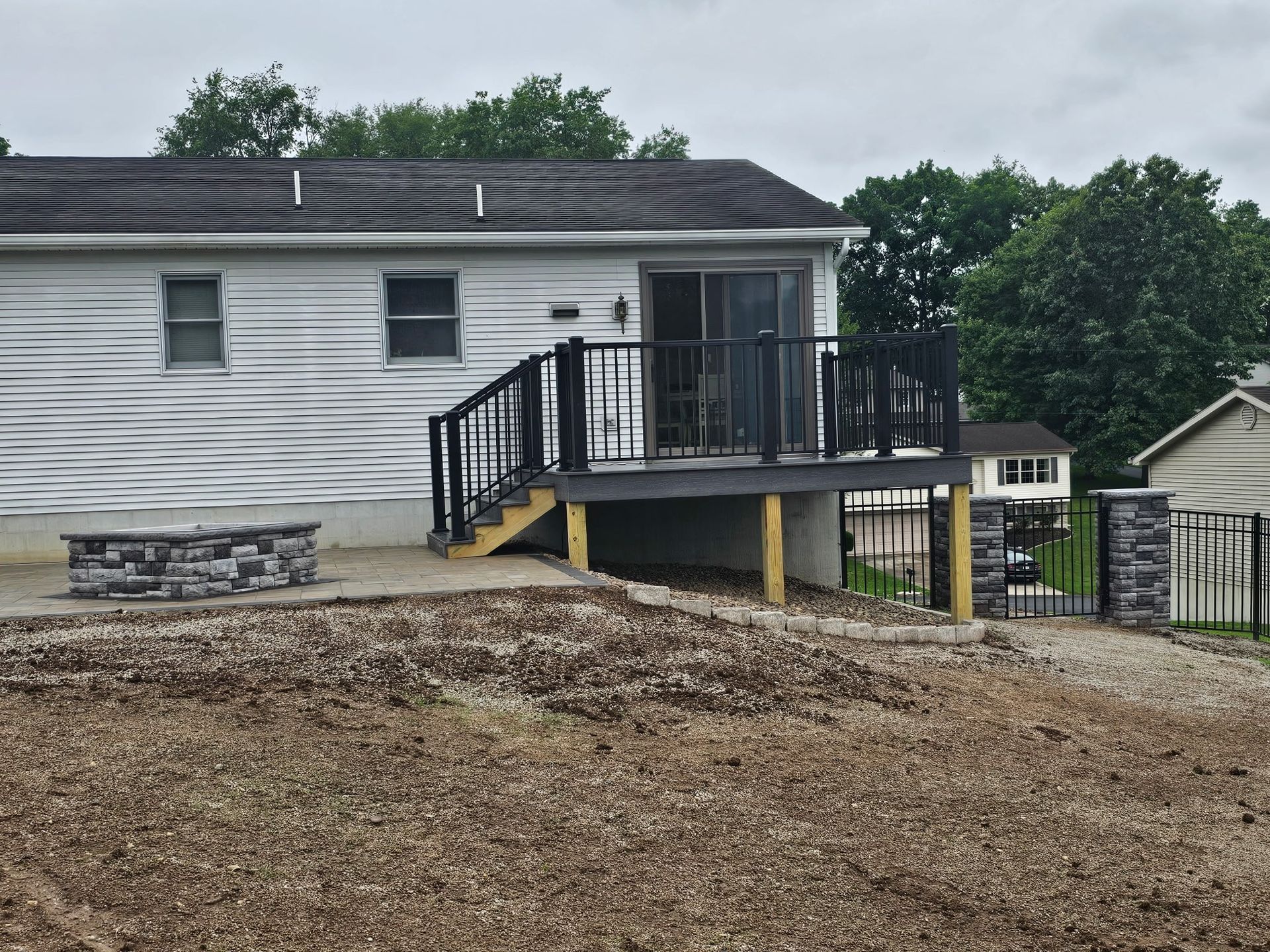 White house with a raised black-railed deck on a gravel lot under cloudy skies