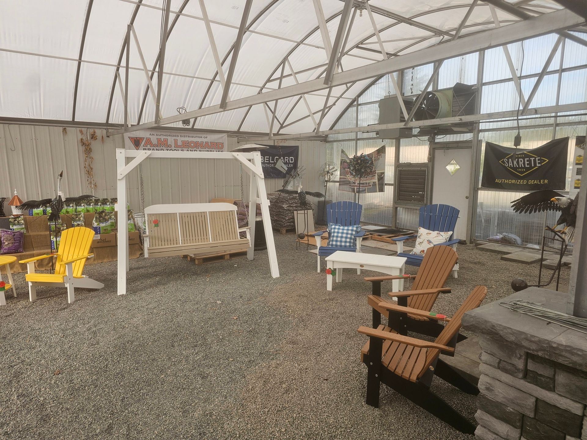 Spacious greenhouse patio with Adirondack chairs, white swing bench, gravel floor, and potted plants.