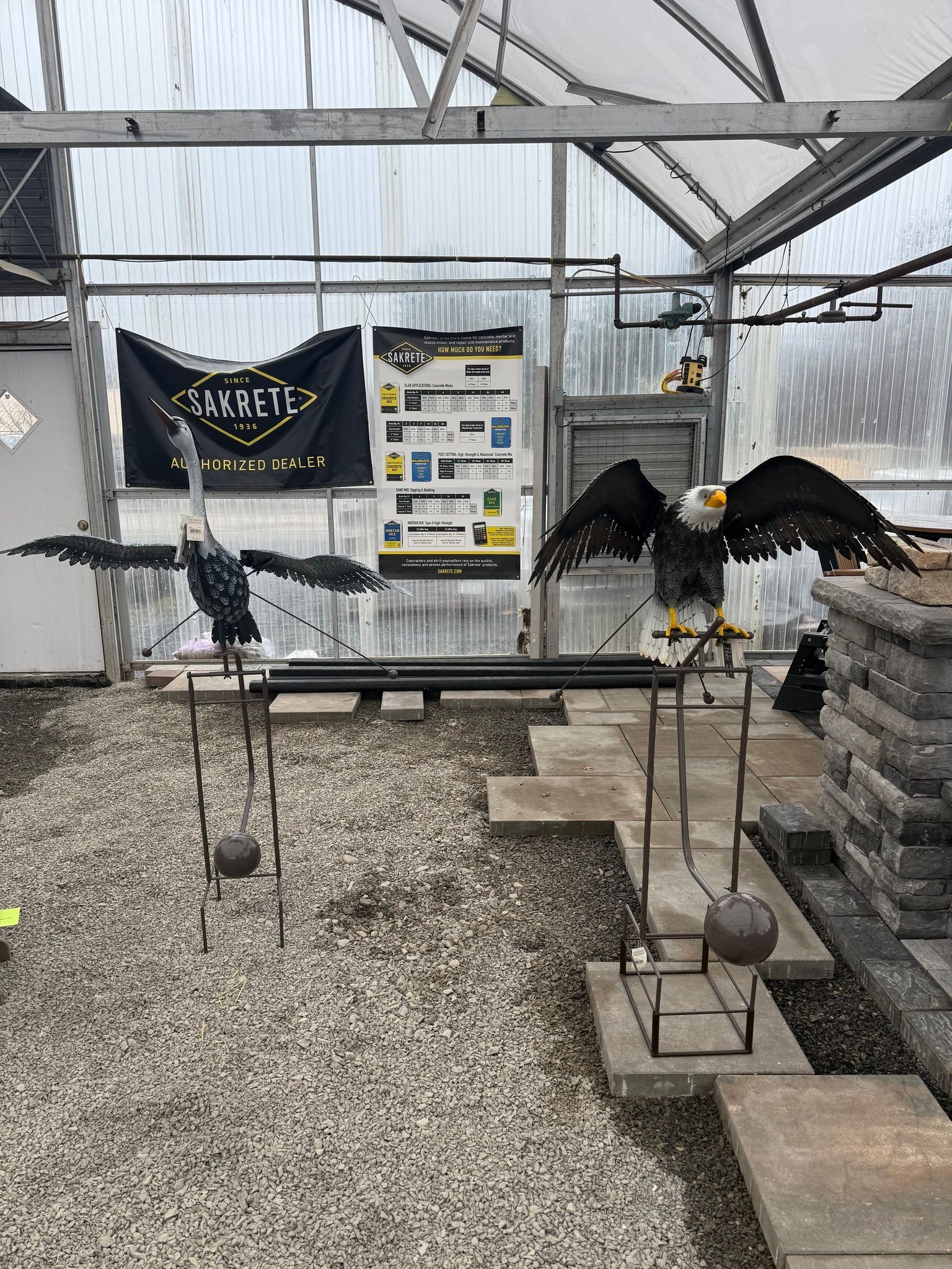 Two black birds perched on stands in a greenhouse exhibit with signs and gravel floor