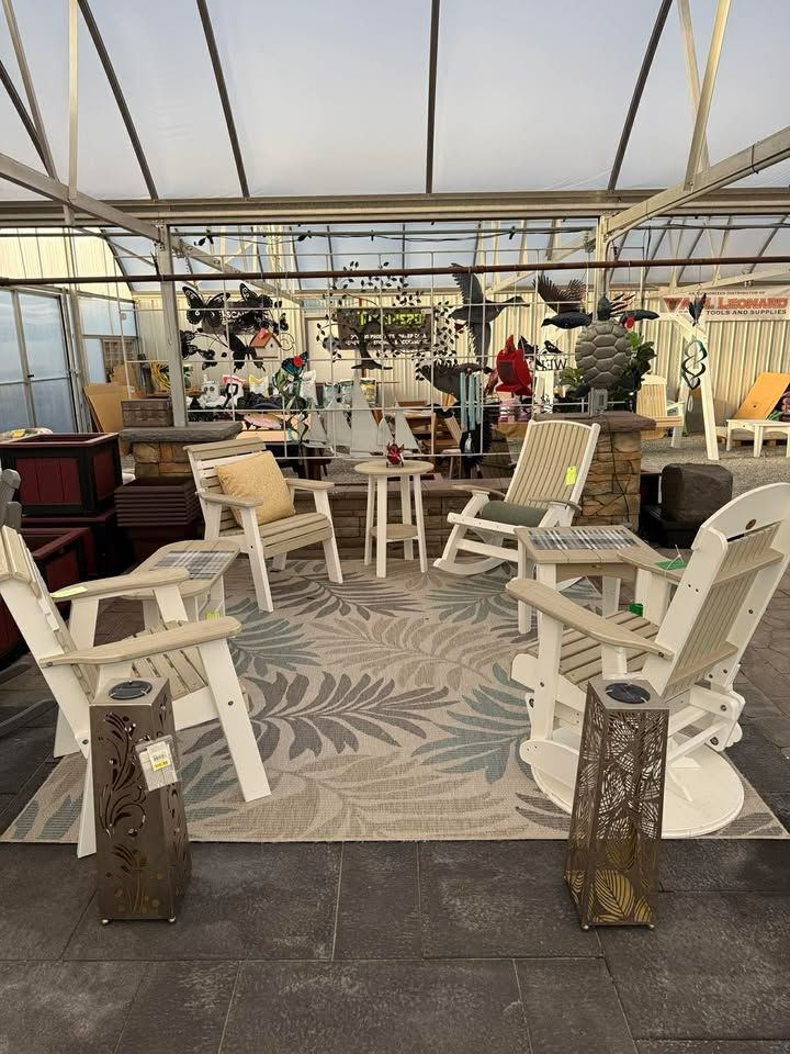 Covered patio seating area with white chairs, patterned rug, and potted plants.