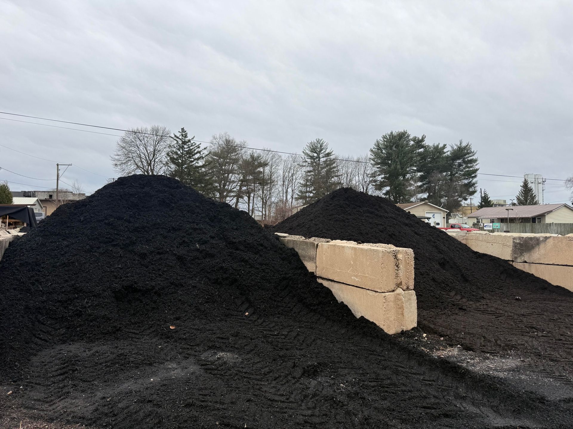 Large piles of black gravel or coal outdoors beside stacked concrete blocks under an overcast sky