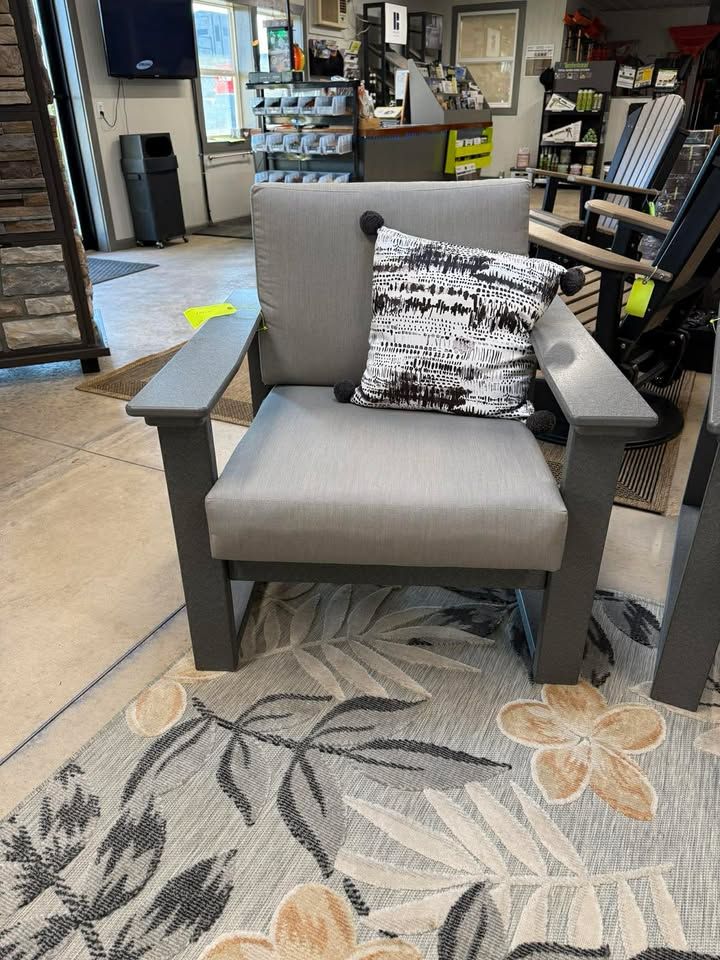 Gray armchair with patterned pillow on a floral rug in a store showroom
