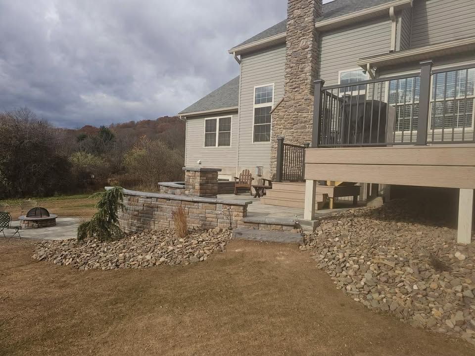 Backyard patio with stone steps, raised deck, and gravel landscaping under a cloudy sky