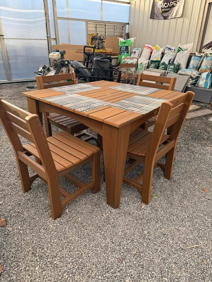 Wooden patio dining set with four chairs in a garage or storage area, surrounded by garden supplies.