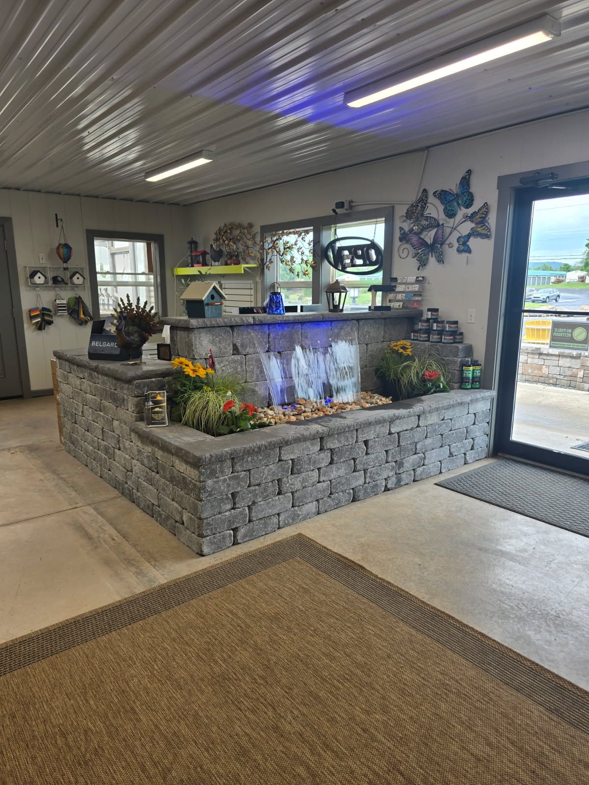Indoor stone fountain with colorful flowers in a bright lobby or resort entrance, with blue butterfly wall art.