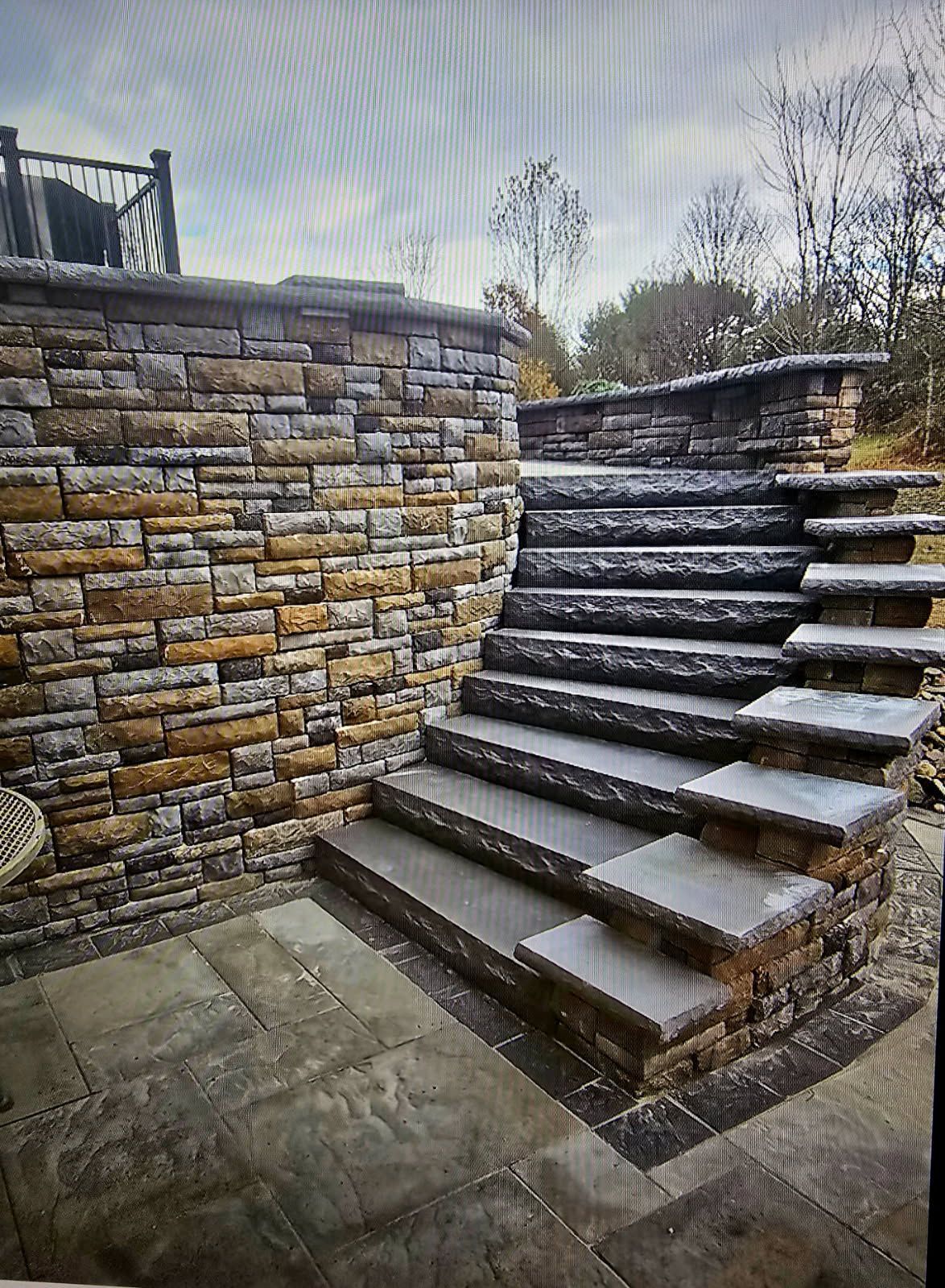 Stone steps beside a stacked-stone retaining wall in an outdoor courtyard, leading up to a higher level