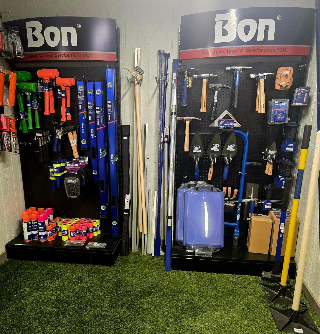 Bon-branded hardware display racks with tools, hoses, and supplies on artificial grass floor indoors