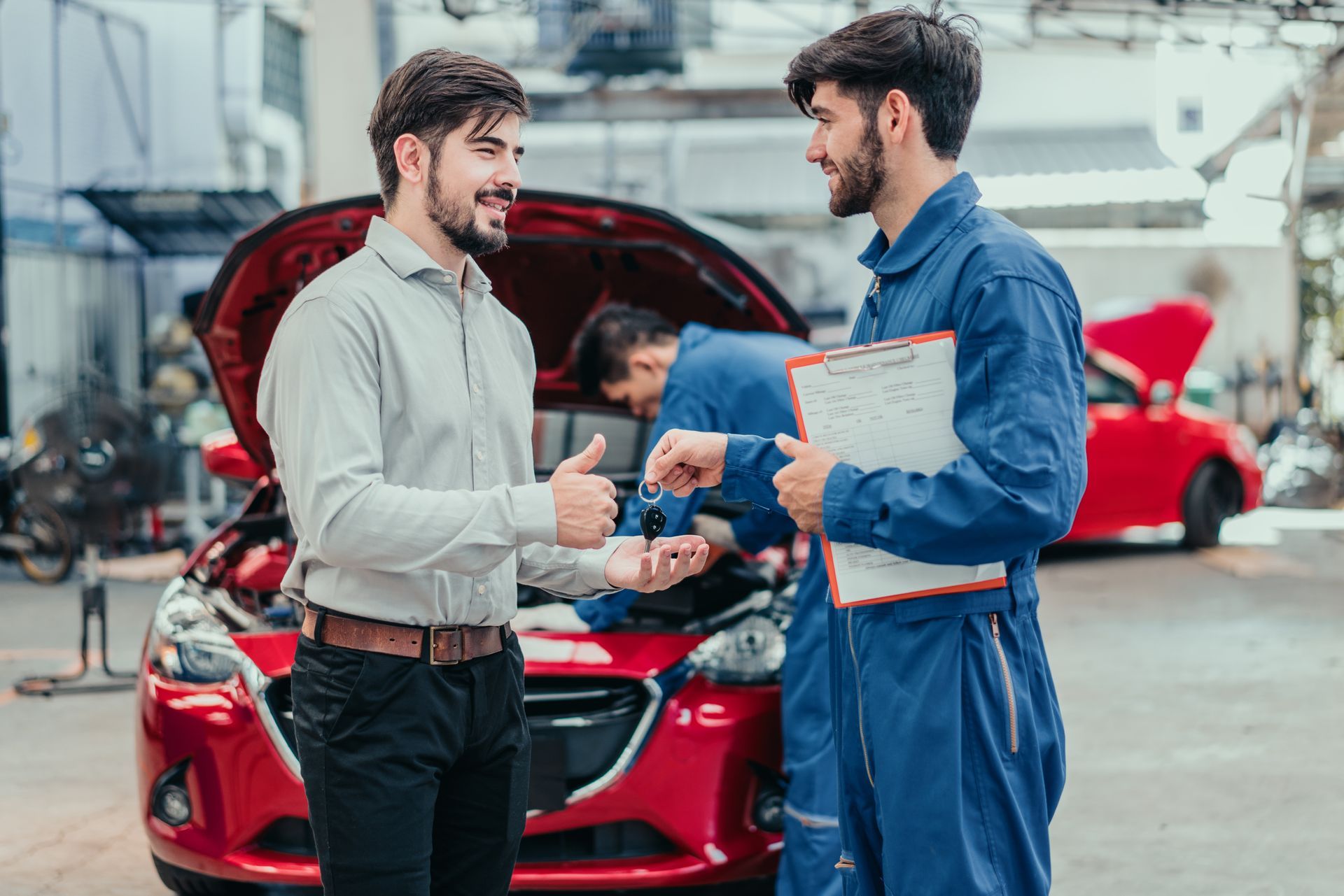 Mechanic and customer shaking hands beside a red car in a garage