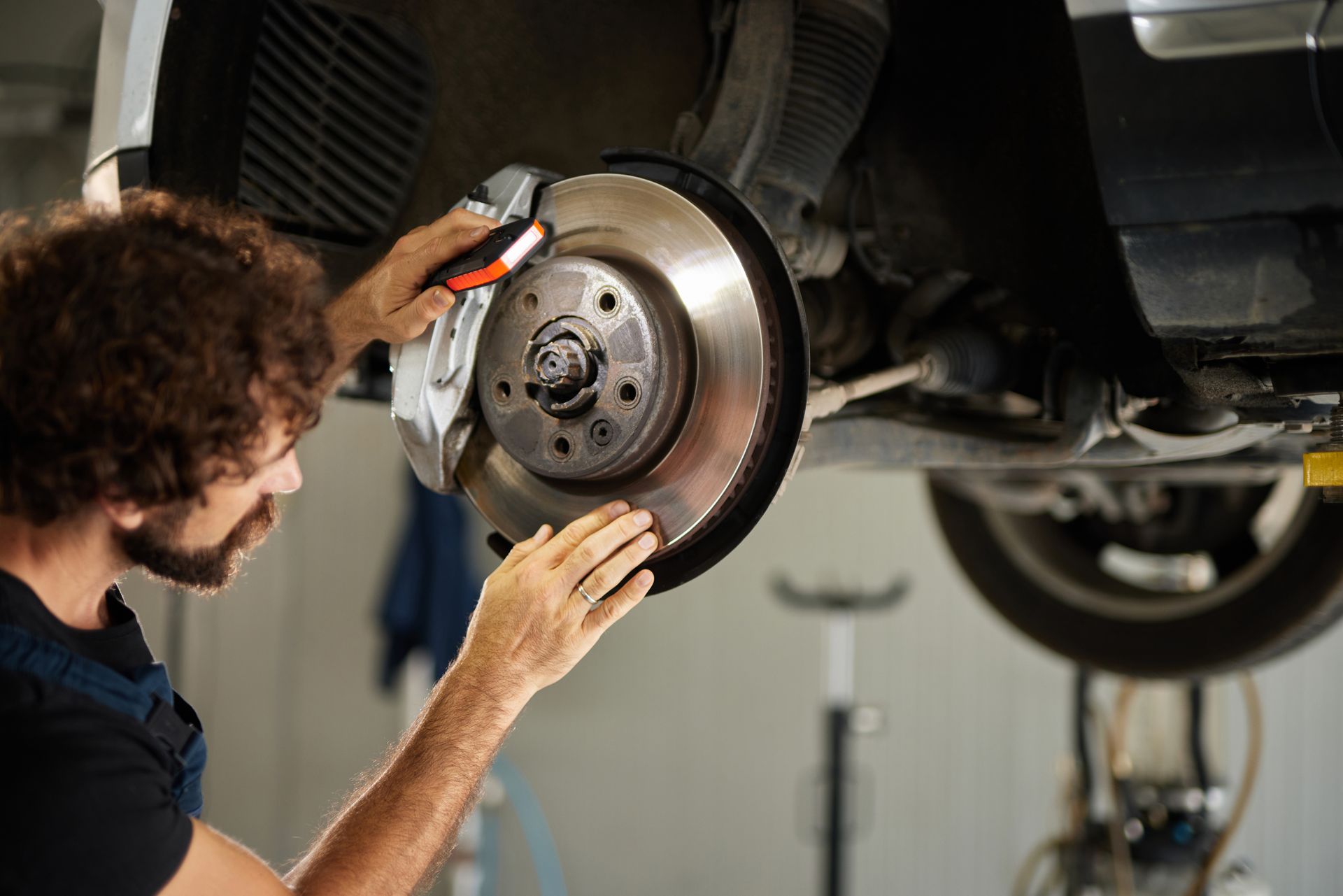 Mechanic inspecting a car’s brake rotor on a lift in an auto repair shop