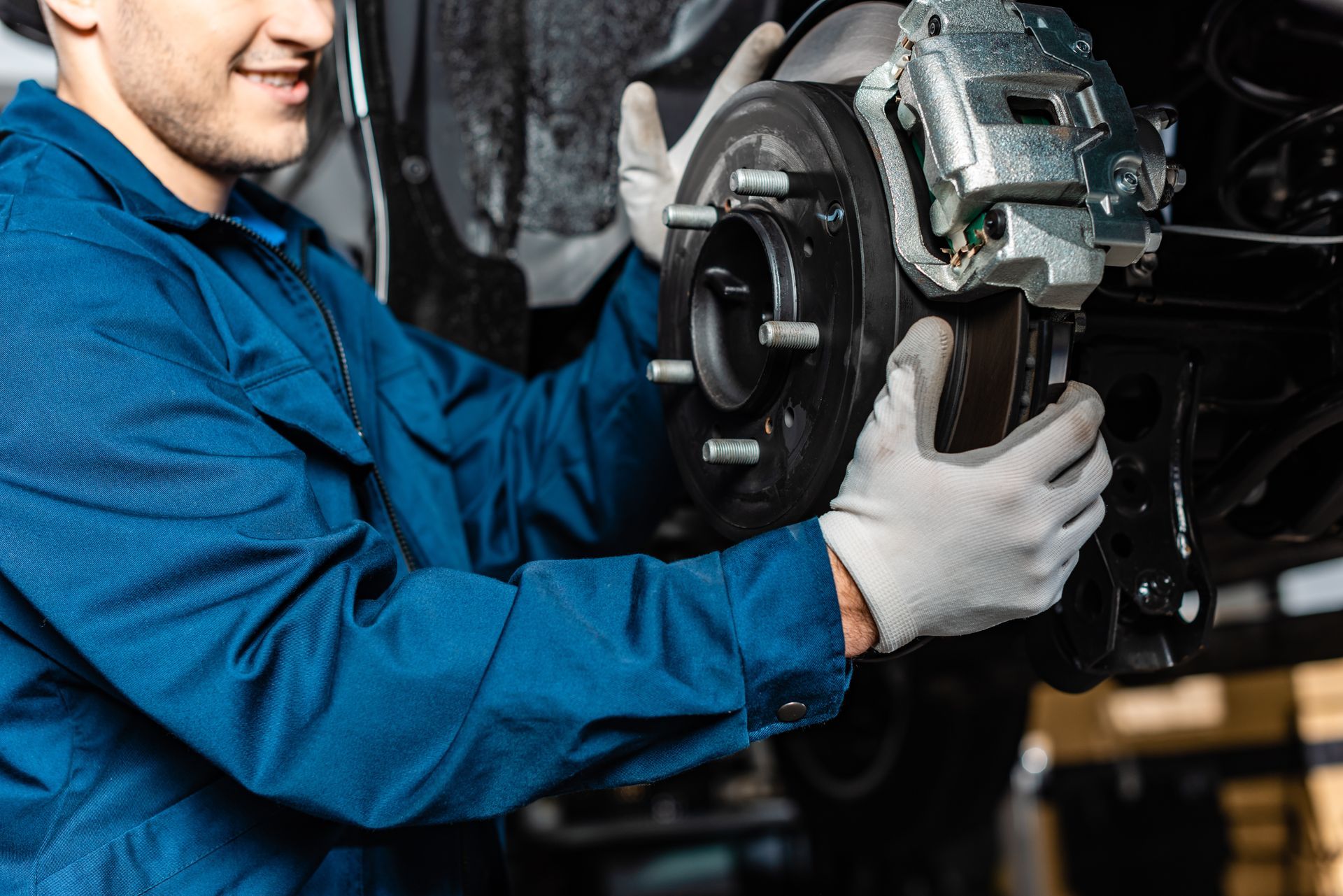 Worker installing a brake rotor and caliper on a car wheel hub in a repair shop.