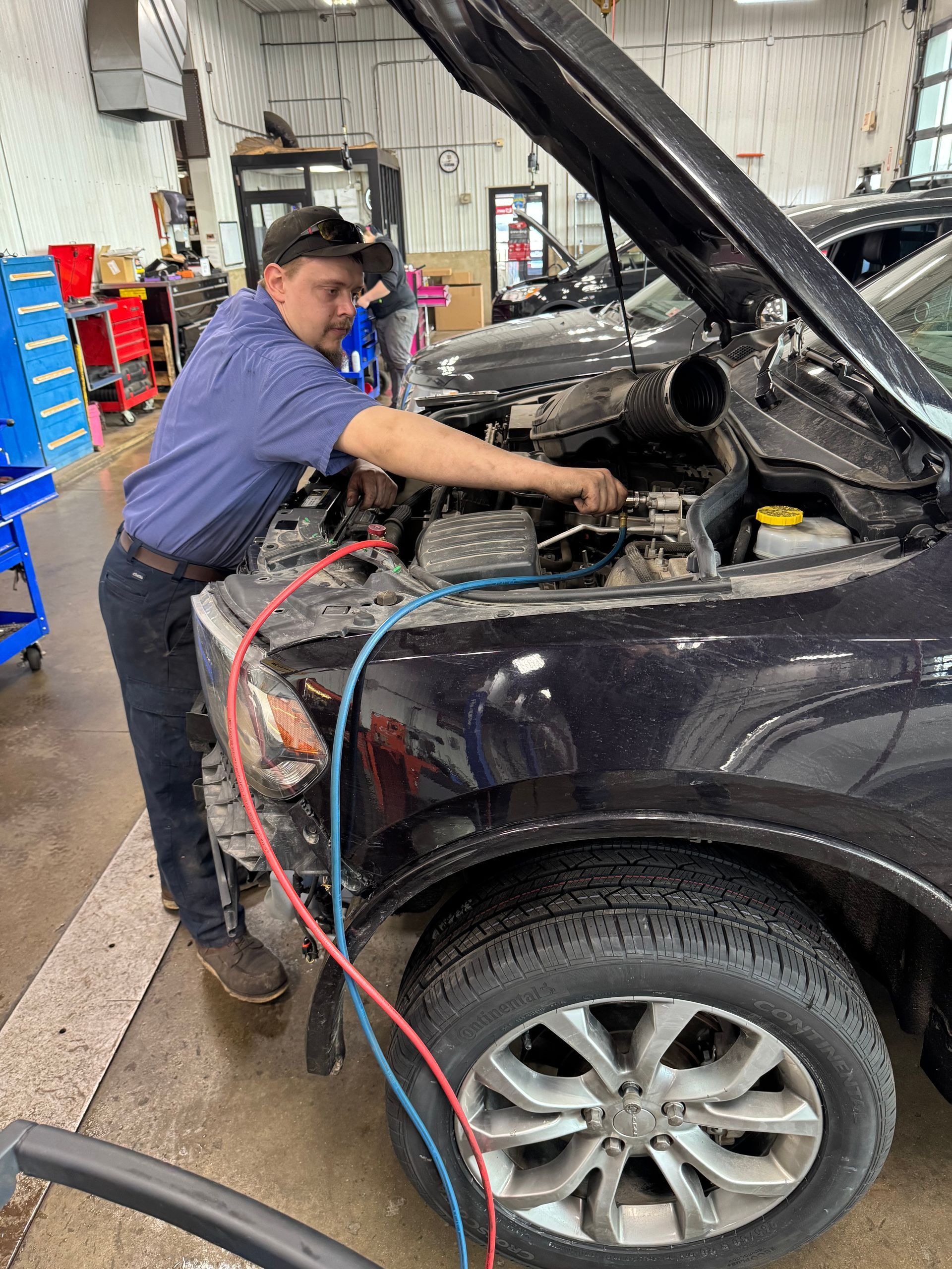 Mechanic working under open hood of a black SUV in a garage, with hoses attached to the engine.