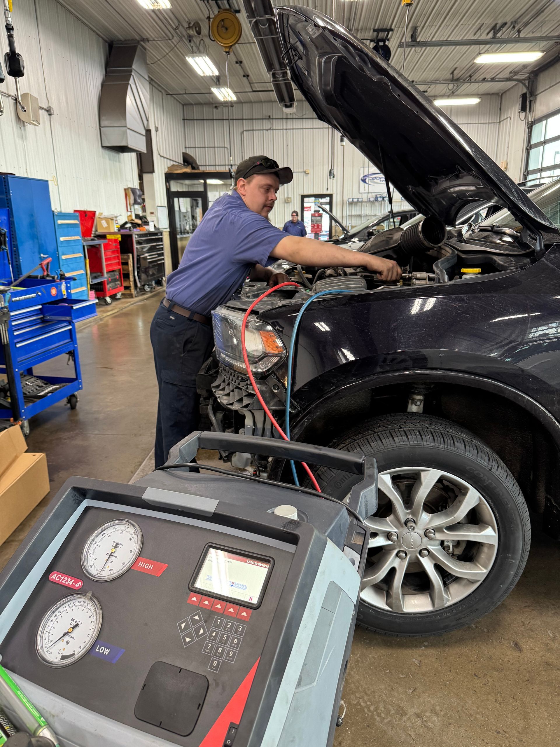 Mechanic inspecting a black SUV with hood open, connected to diagnostic equipment in an auto shop