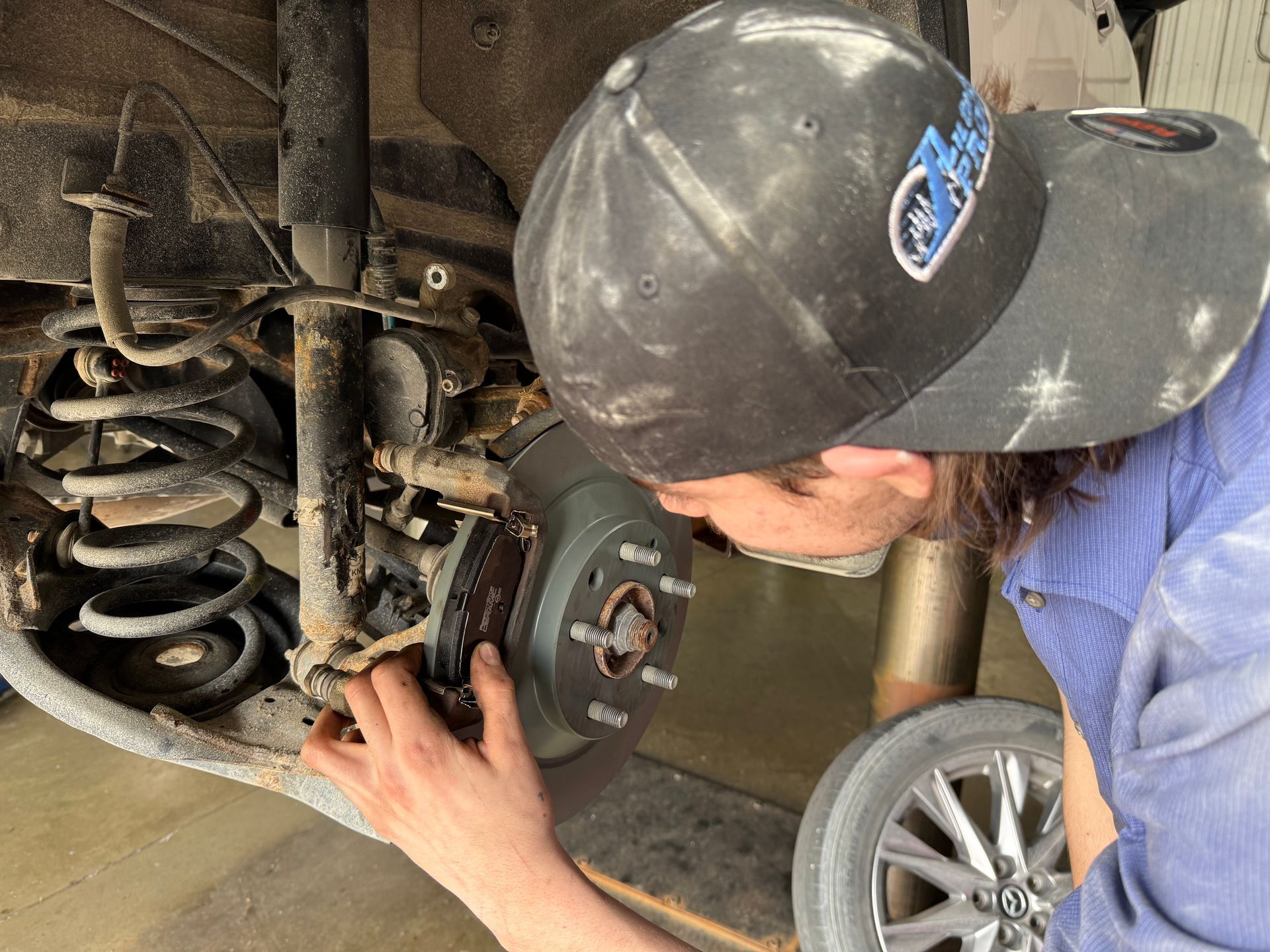 Mechanic inspecting a car’s rear suspension and brake assembly under the wheel well