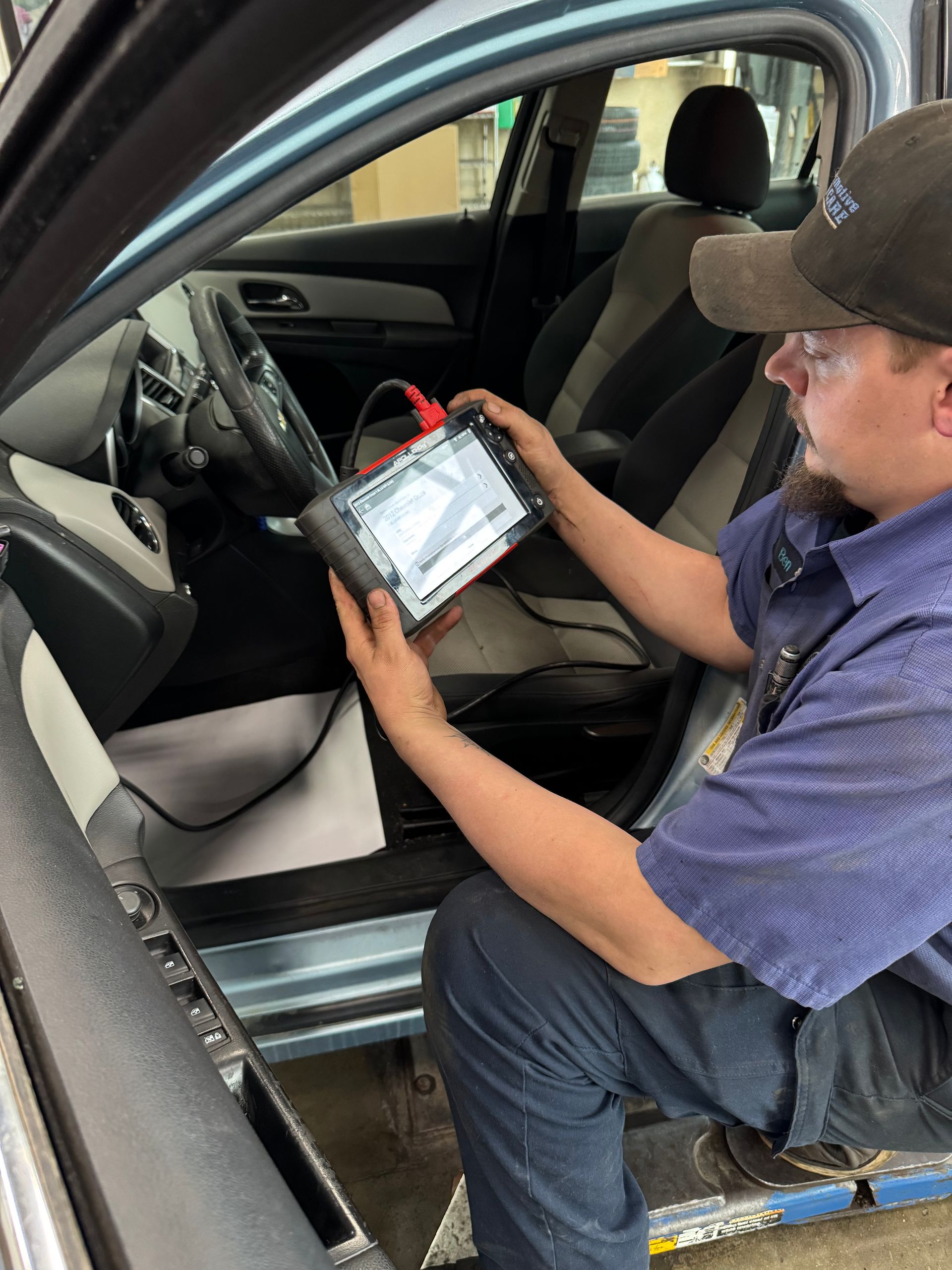 Technician using a tablet to inspect a car’s interior from the open driver’s door