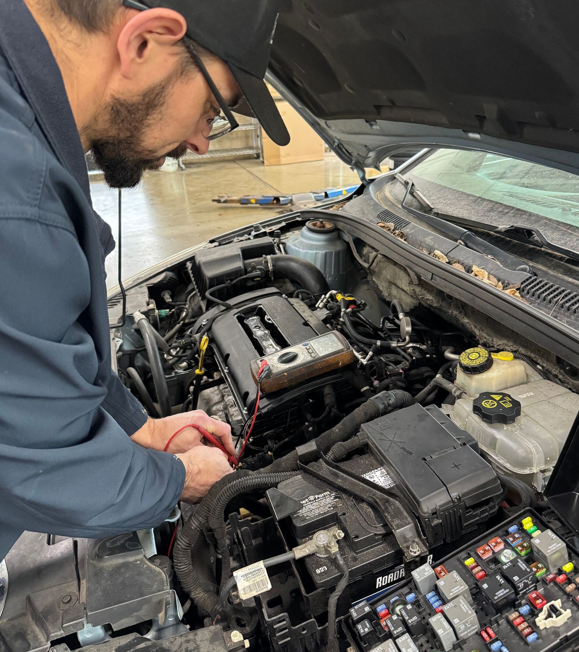 Mechanic inspecting a car engine bay with the hood open and fuse box visible