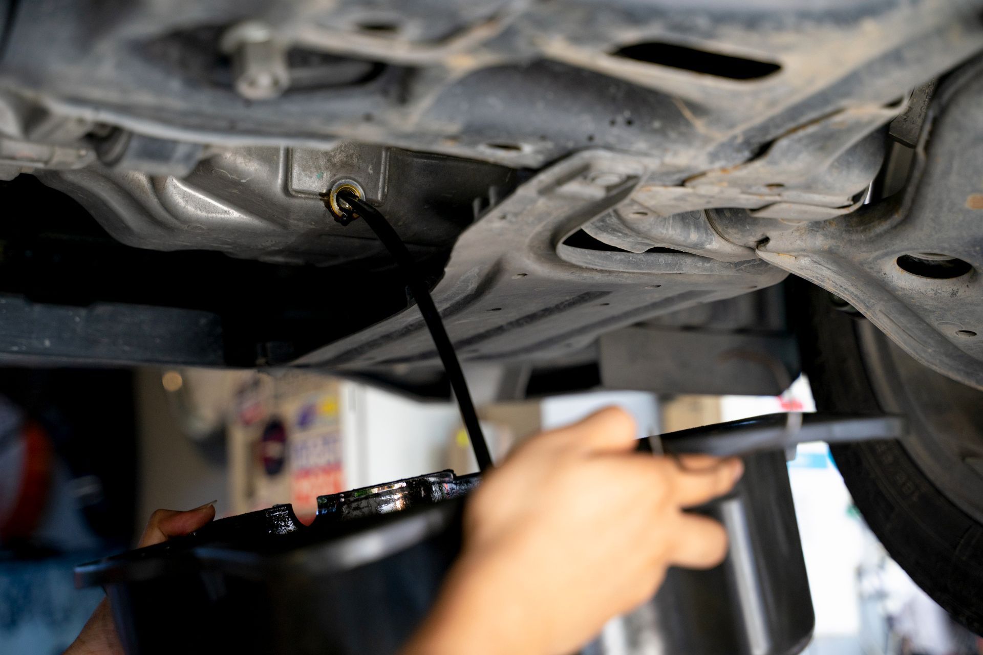 Mechanic draining oil from a car’s undercarriage with a black pan underneath