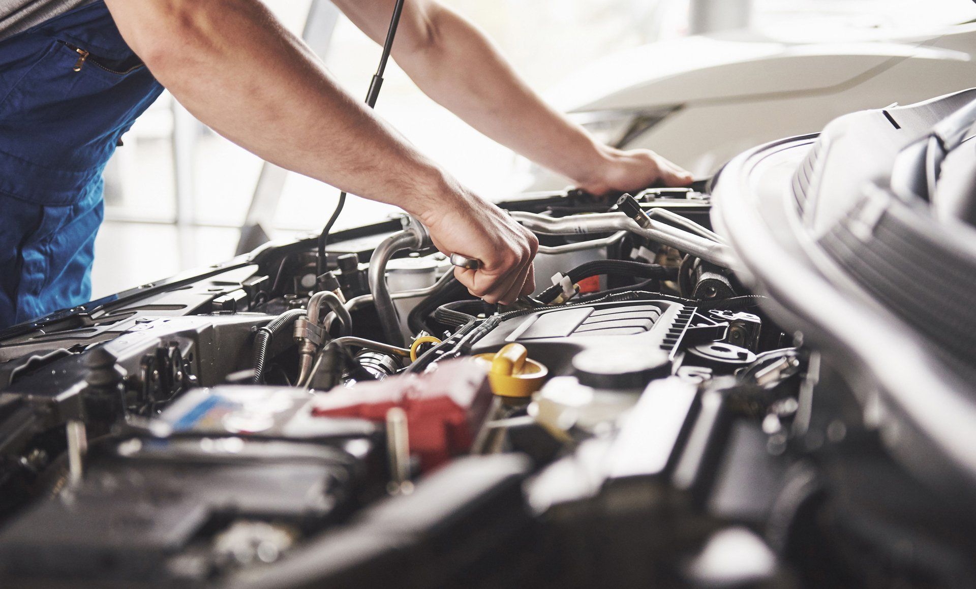 Mechanic working under an open car hood in a garage, inspecting engine components