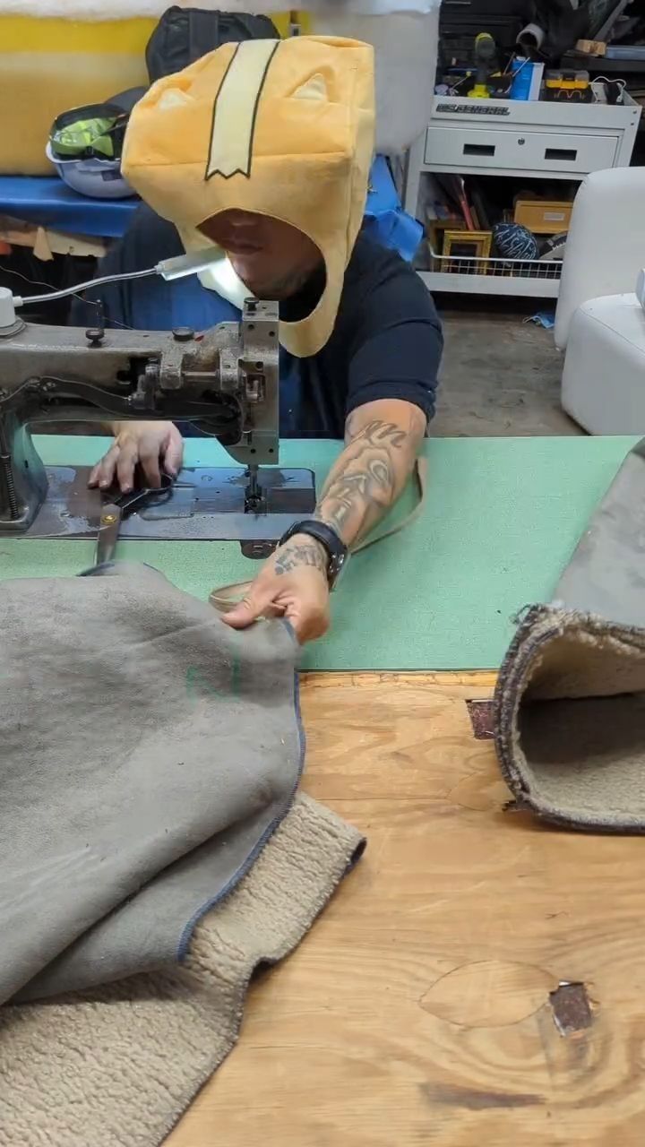 Person at a sewing machine cutting green fabric on a worktable, with gray material in the foreground.
