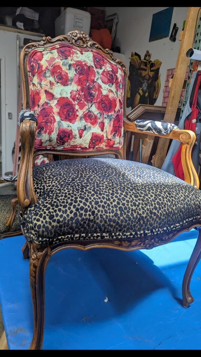 Vintage upholstered armchair with floral back and leopard-print seat on a blue floor, in a cluttered room