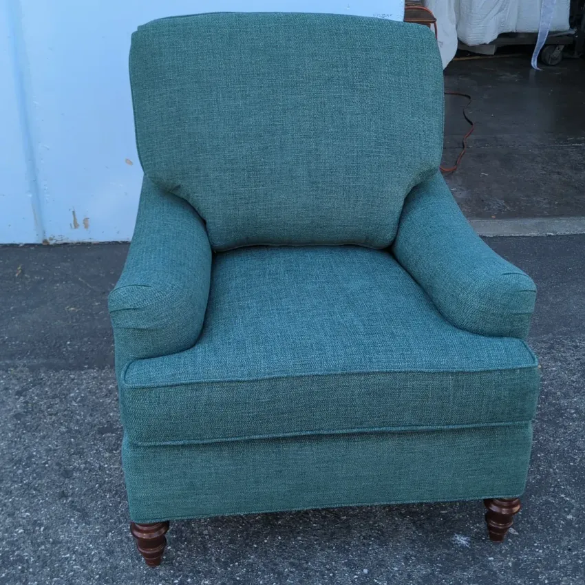 Teal upholstered armchair with rolled arms and wooden feet, shown against a white wall.