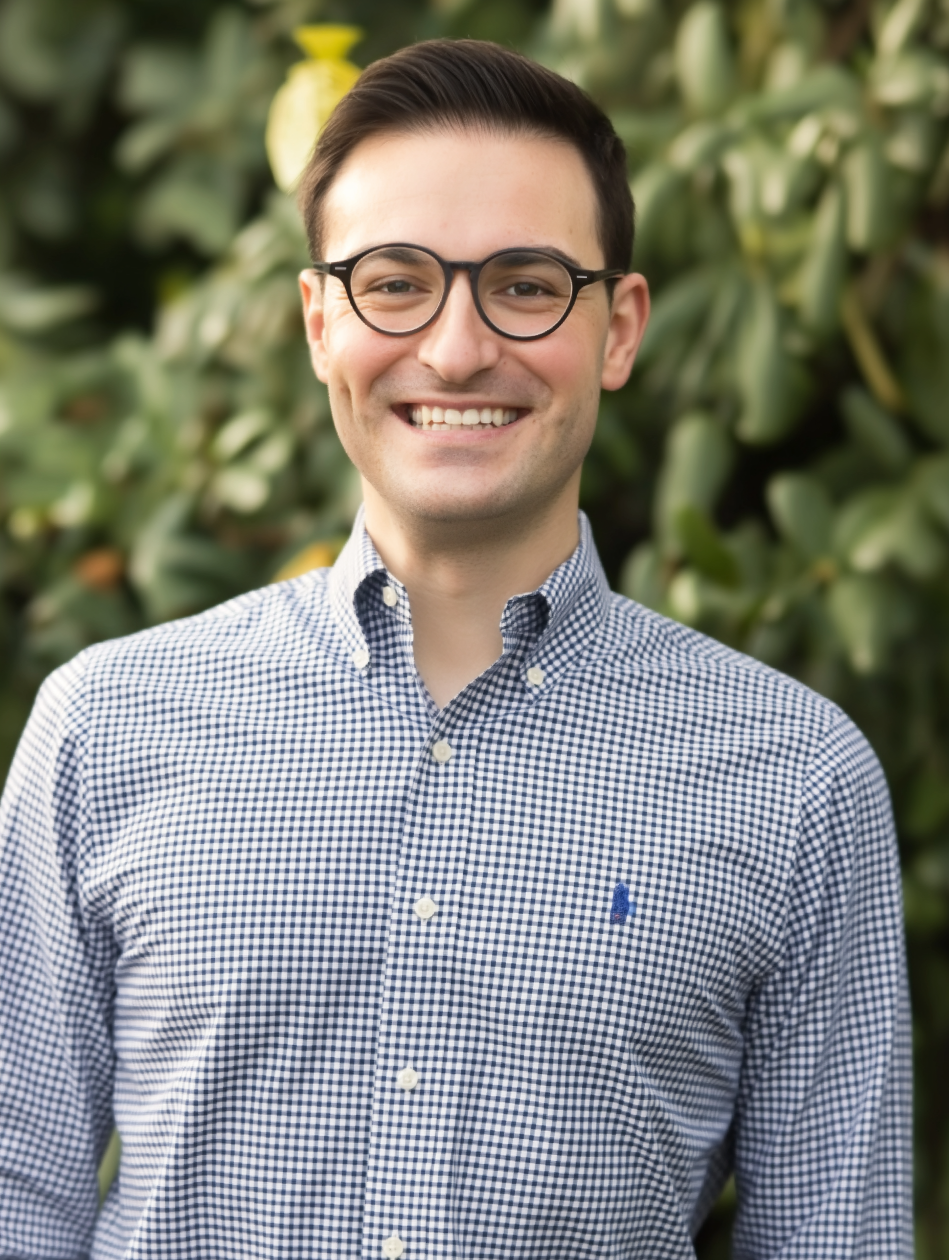 Man in a suit smiles, wearing glasses, dark background.