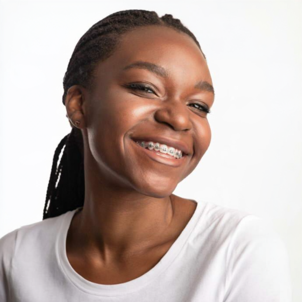 Smiling woman with braided hair and braces, wearing a white shirt against a light background