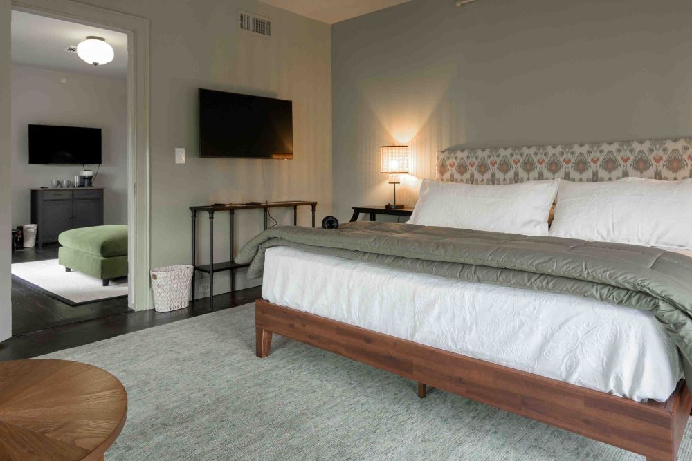 Bedroom with bed, TV, and open doorway to another room with a green ottoman.