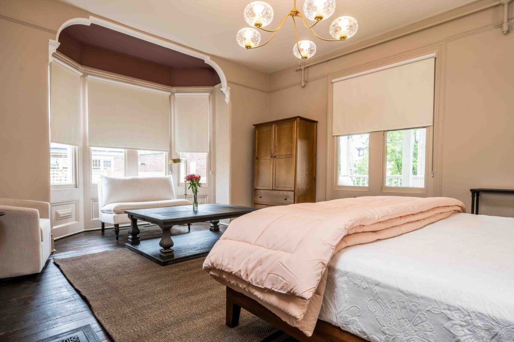 Bedroom with bed, seating area, large windows, and a wooden wardrobe.