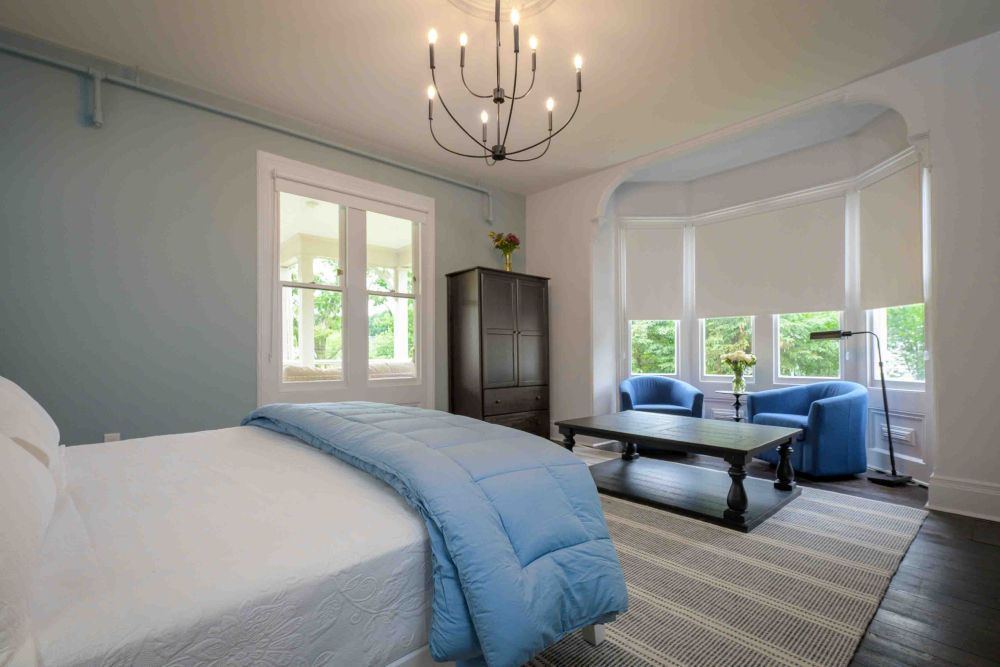 Bedroom with a bed, blue accents, large windows, and a sitting area with blue chairs and a coffee table.