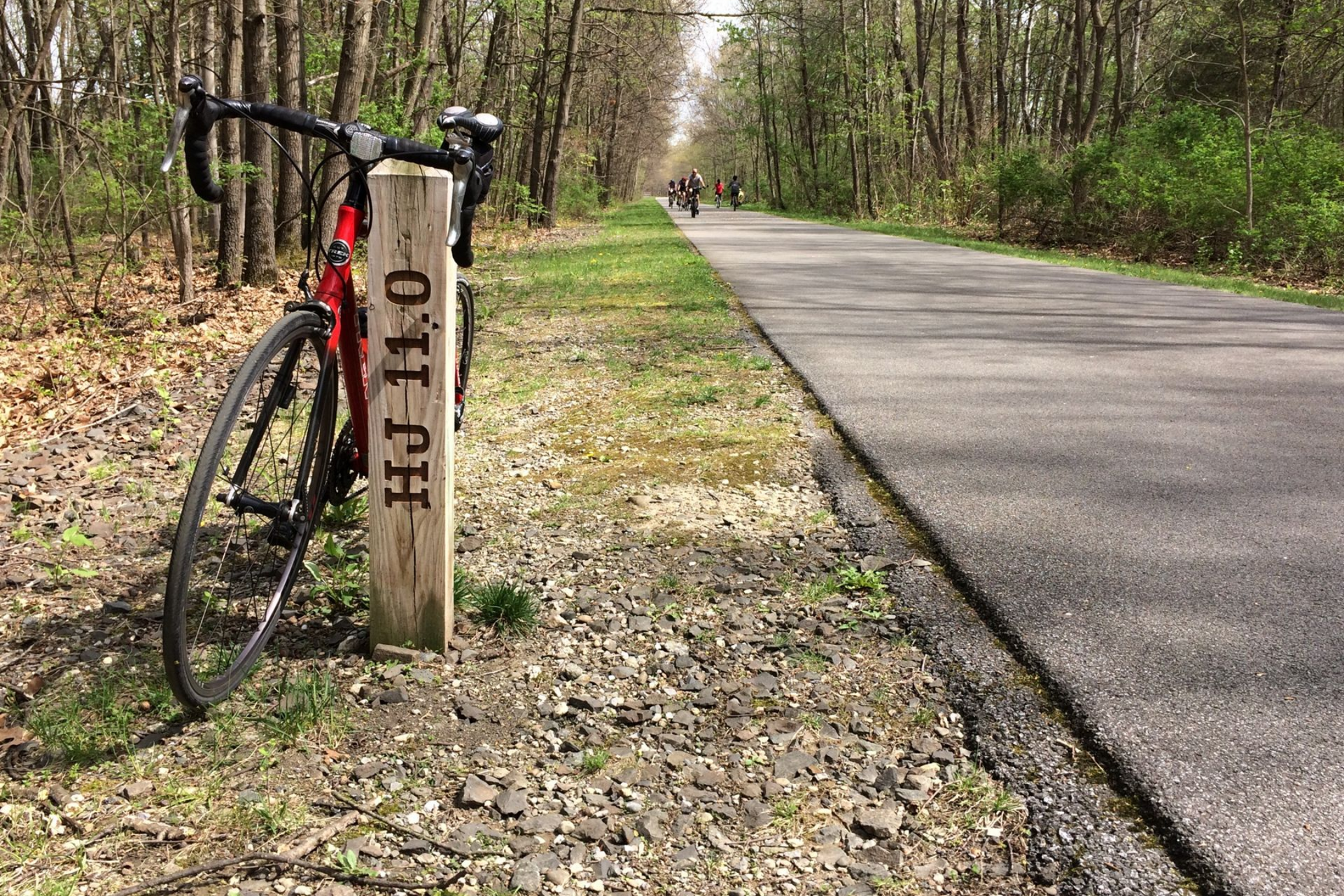 Red bicycle next to a wooden post on a paved path in a forest.