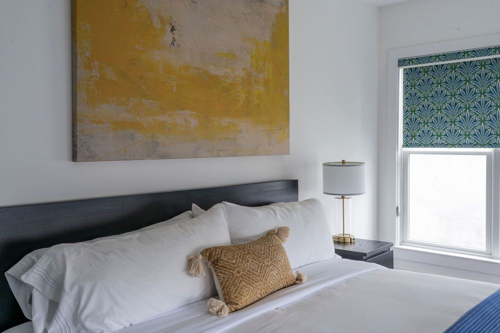 Bedroom with white walls, king bed, yellow artwork, and dark nightstands.