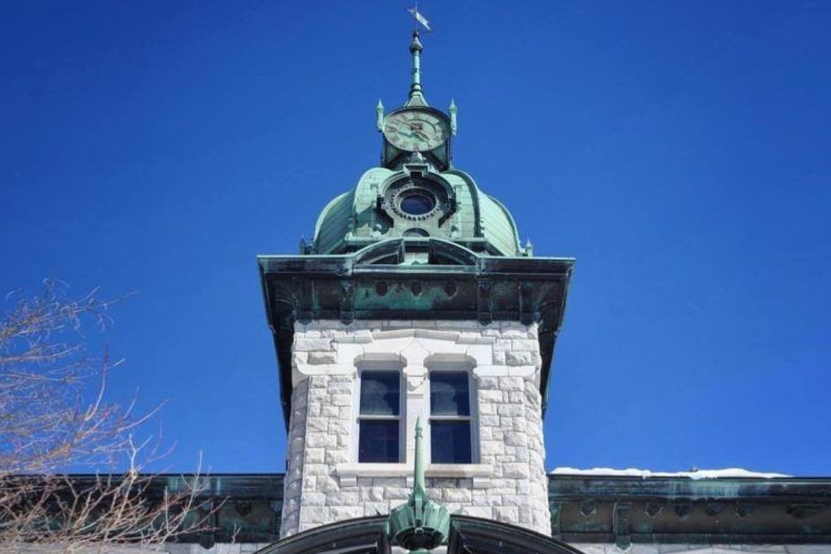 Stone clock tower with green dome against a blue sky.