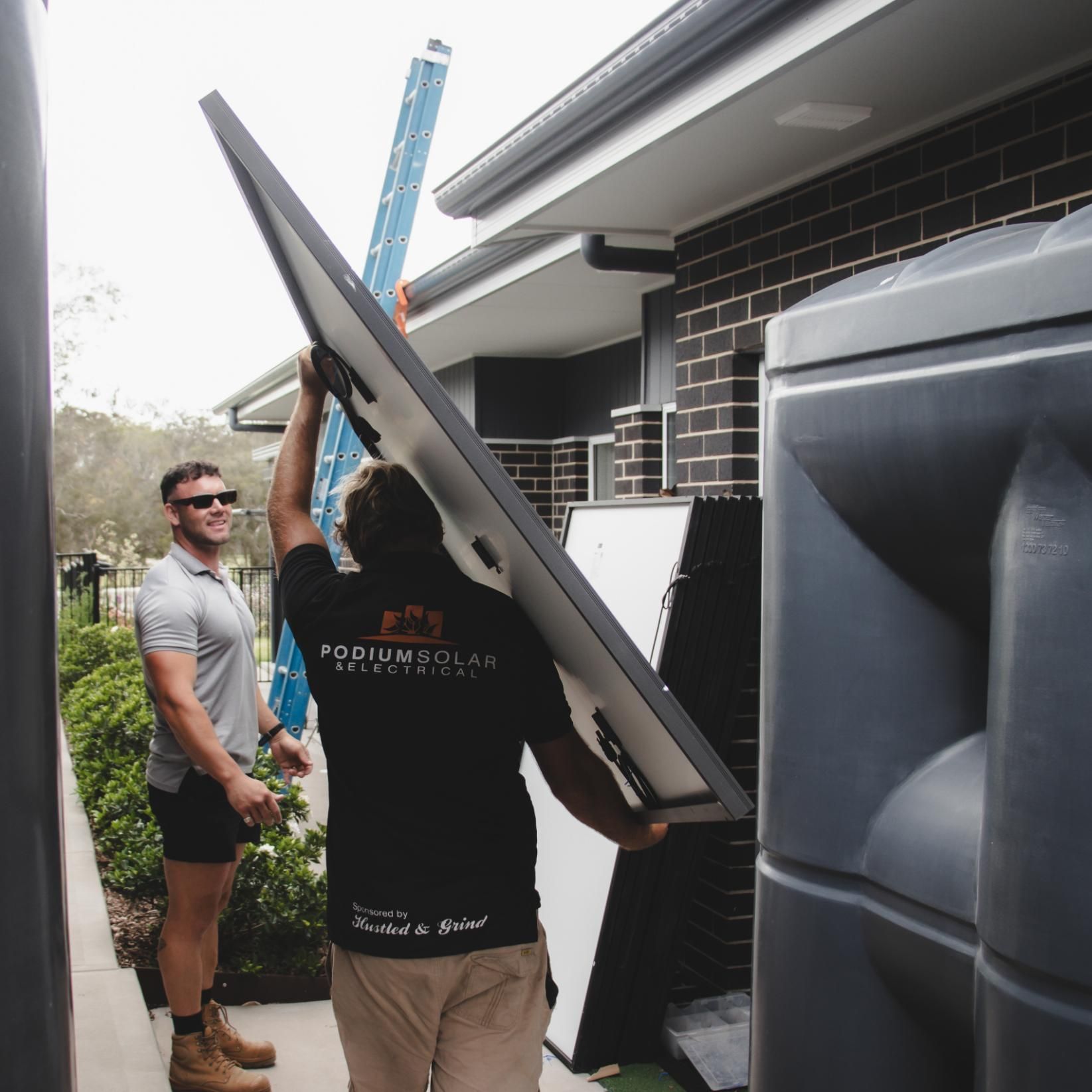A Man Wearing a Podium Solar Shirt Is Carrying a Solar Panel — Podium Solar in Cameron Park, NSW