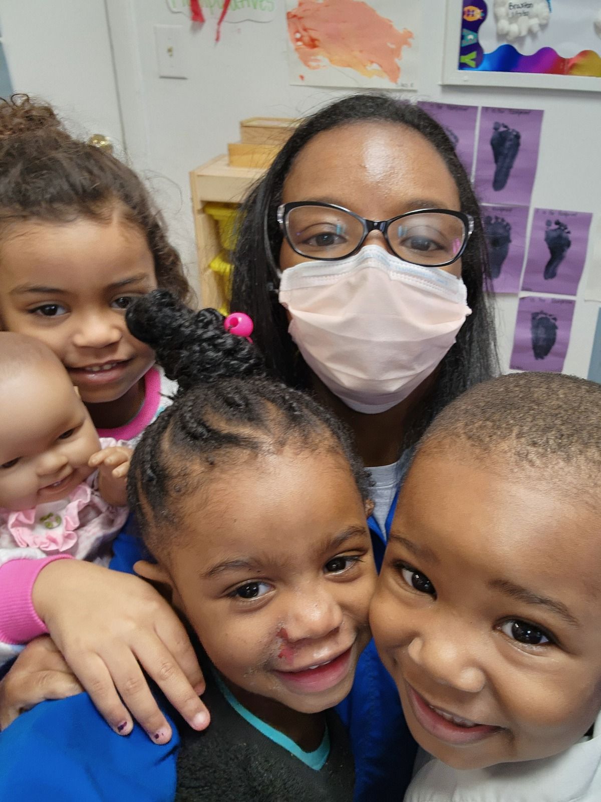 Teacher wearing a mask surrounded by smiling children in a classroom