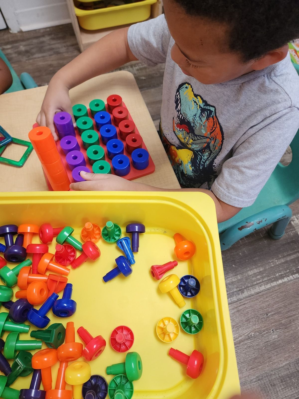 Child sorting colorful toy pieces into a container while seated at a table.