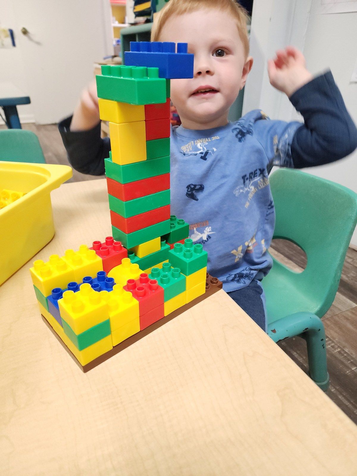 Child smiling beside a colorful block tower at a classroom table