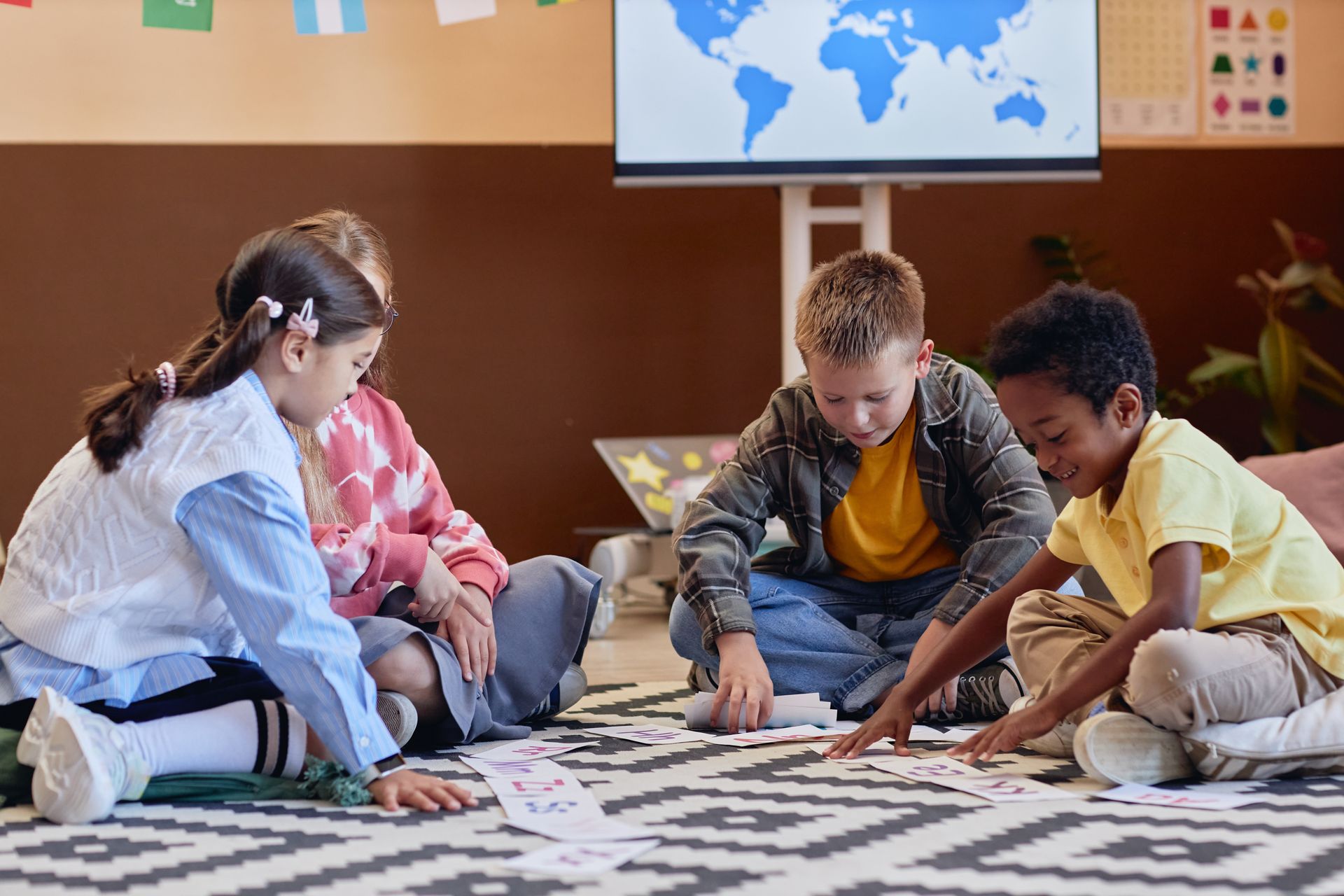 Children playing a floor puzzle in a classroom, sitting on a rug with a world map on the wall.