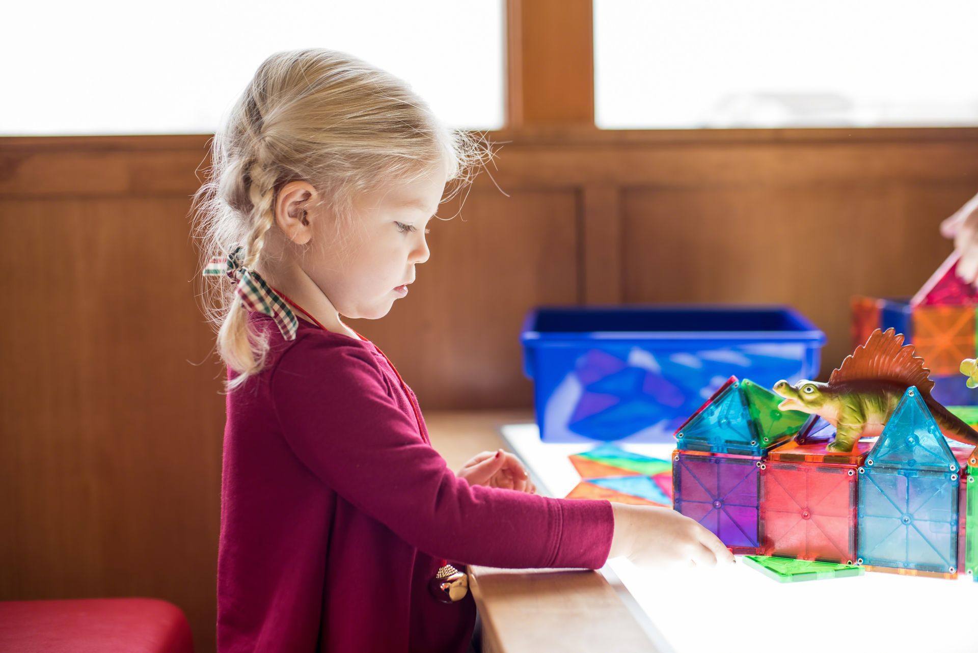 Child in a red sweater looking at colorful geometric toys on a table indoors