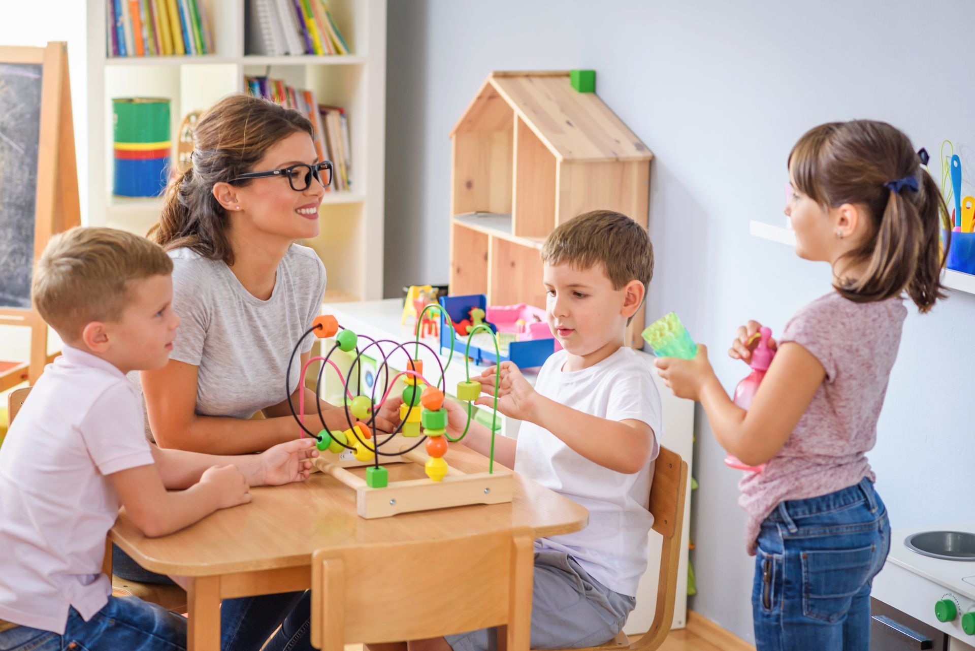 Children and a teacher play with a colorful bead maze at a classroom table