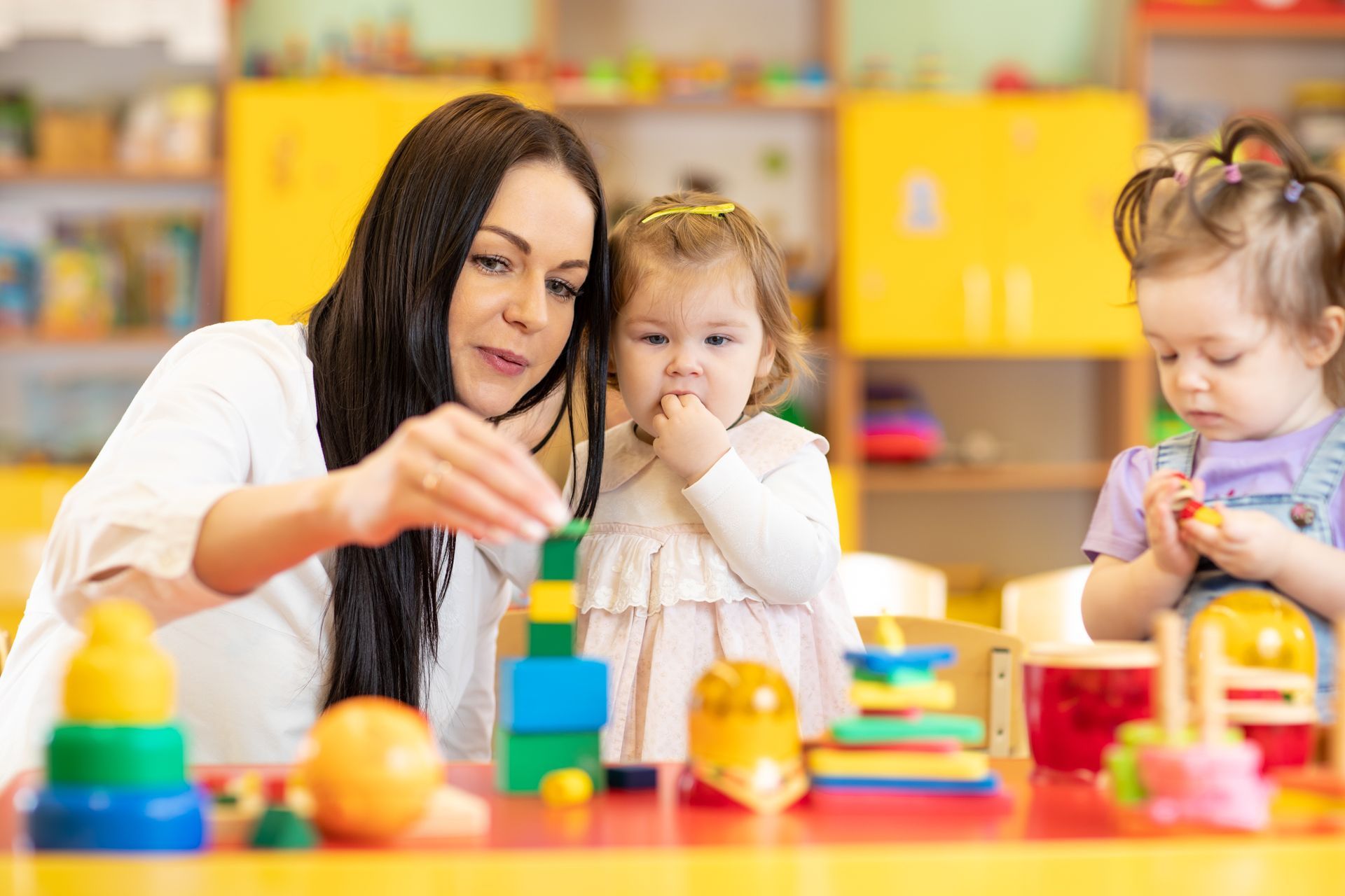 Teacher helping toddlers with colorful blocks in a bright classroom