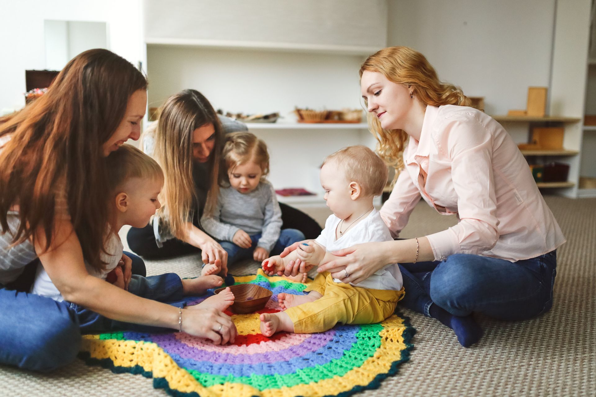 People and children playing with colorful toys on a rug in a bright living room