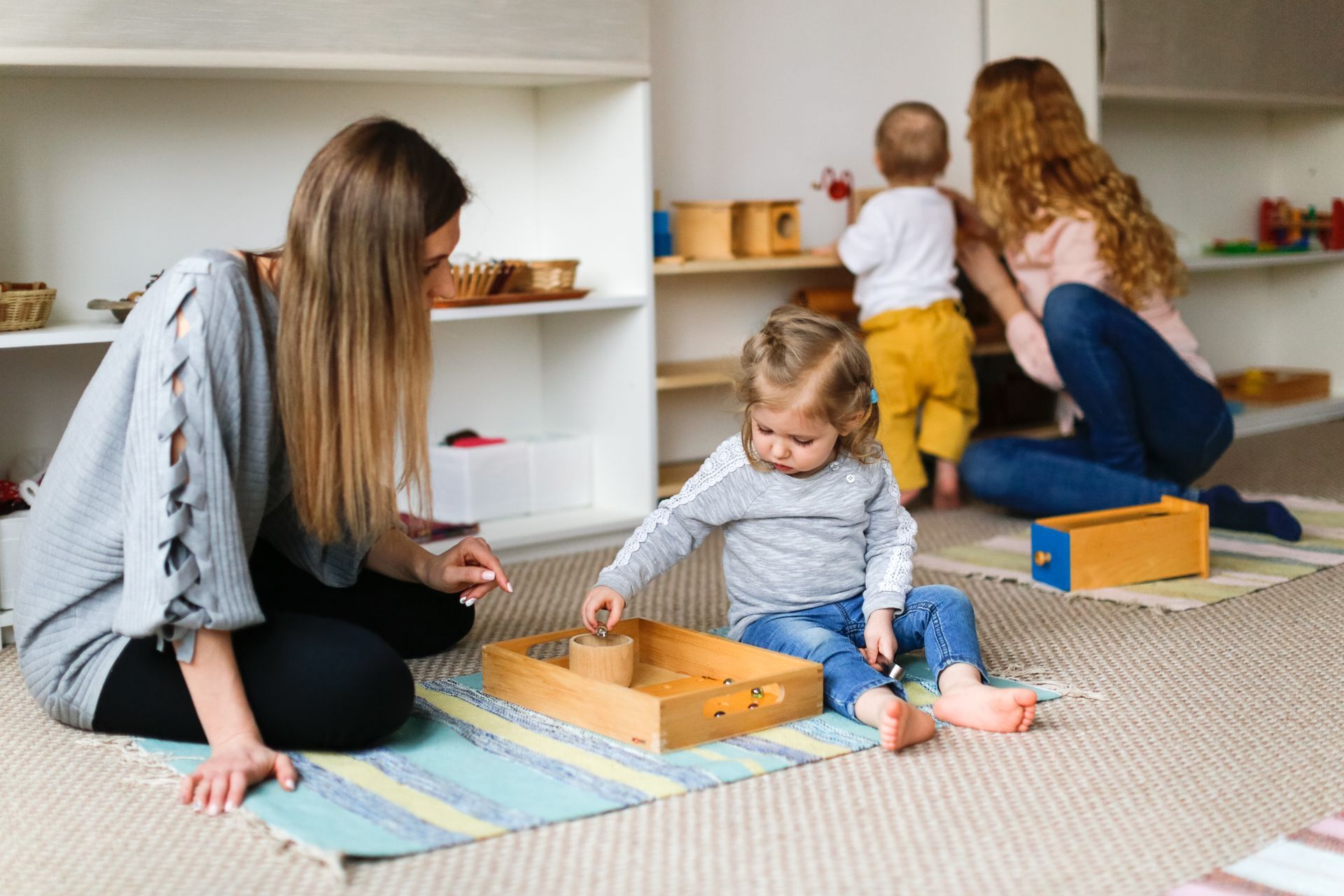 Three children and an adult playing with toys on a carpet in a bright playroom